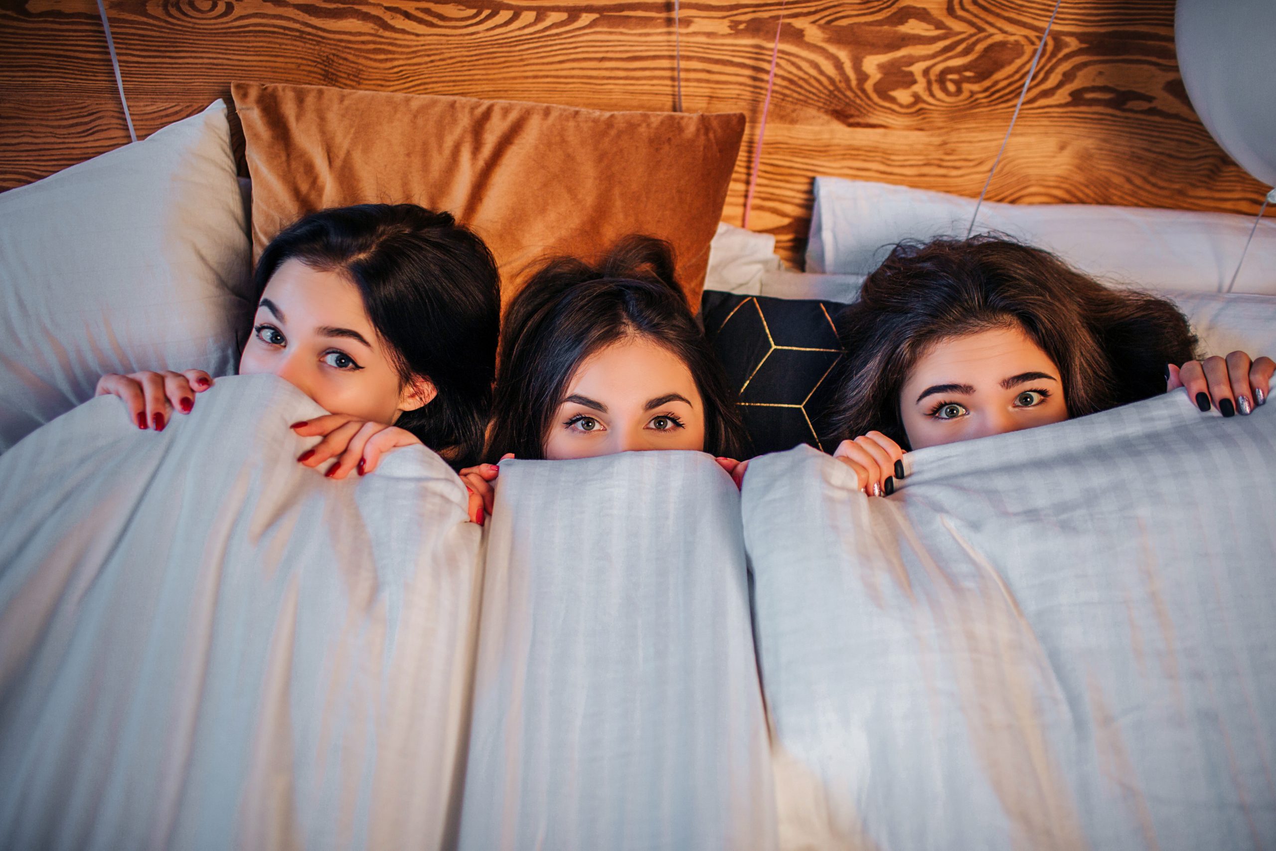 Excited young women covering part of their faces with white blanket