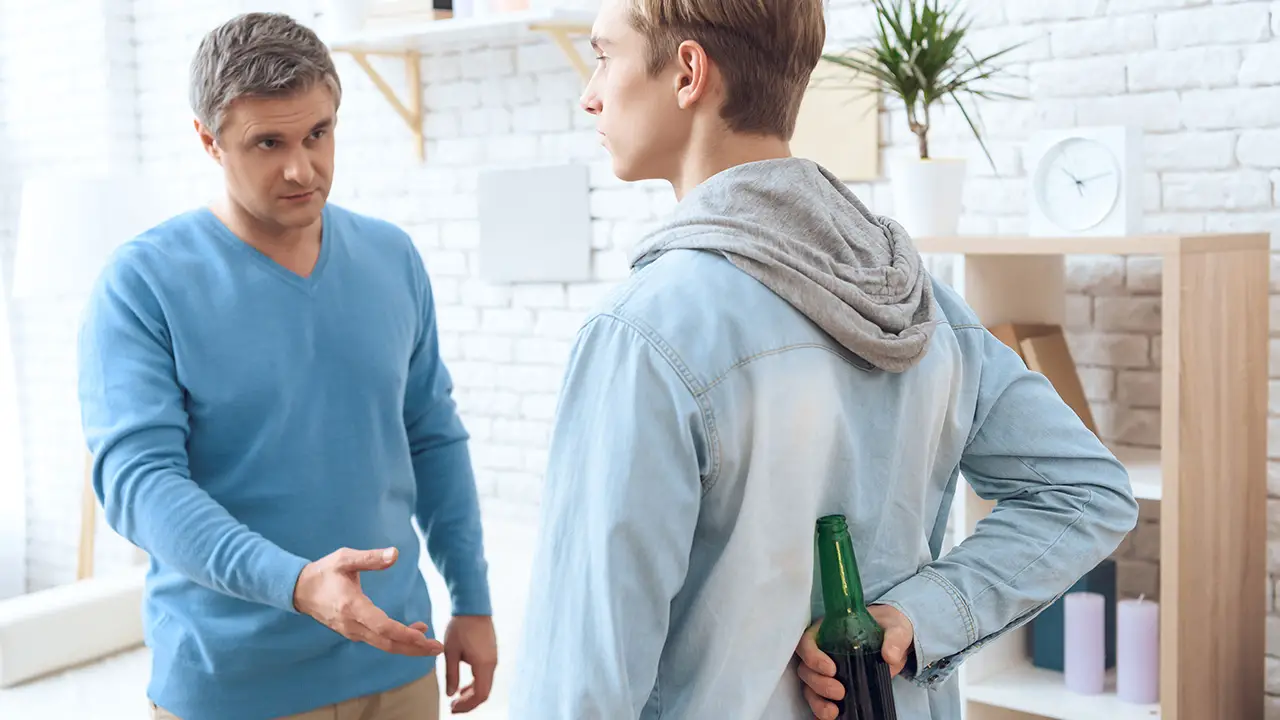 Teenager holds a beer behind his back in front of his father