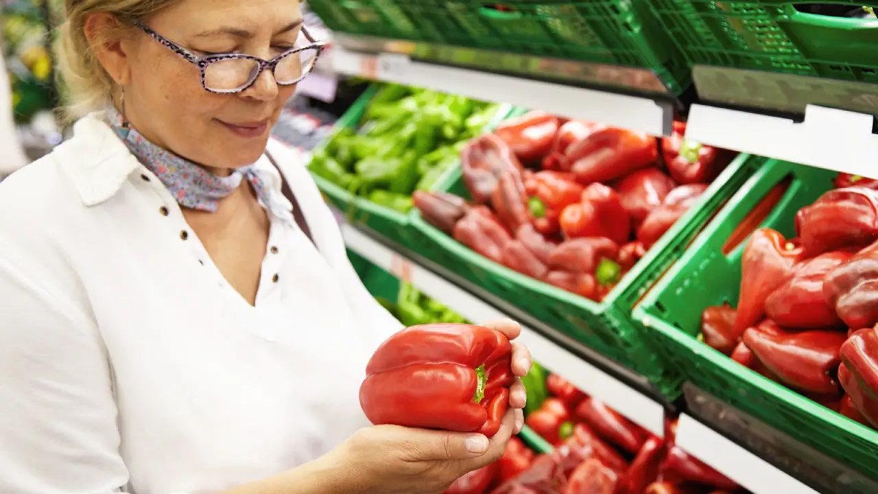 An elderly woman looking at the quality of a bell pepper