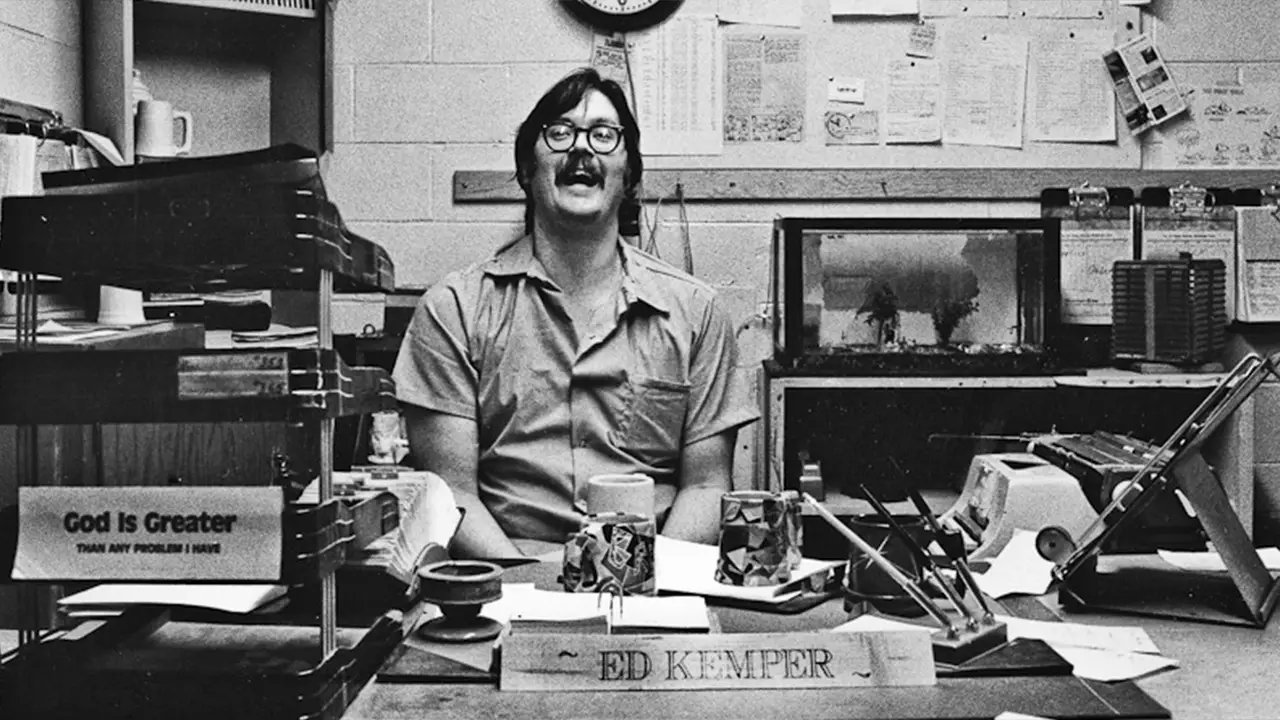 Edmund Kemper sitting down at a desk whilelaughing desk