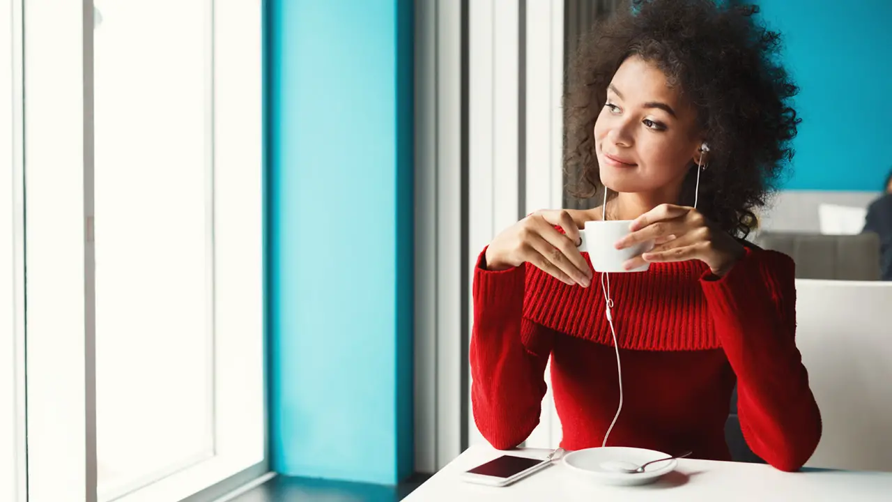 Happy black girl at cafe listening to music and drinking coffee