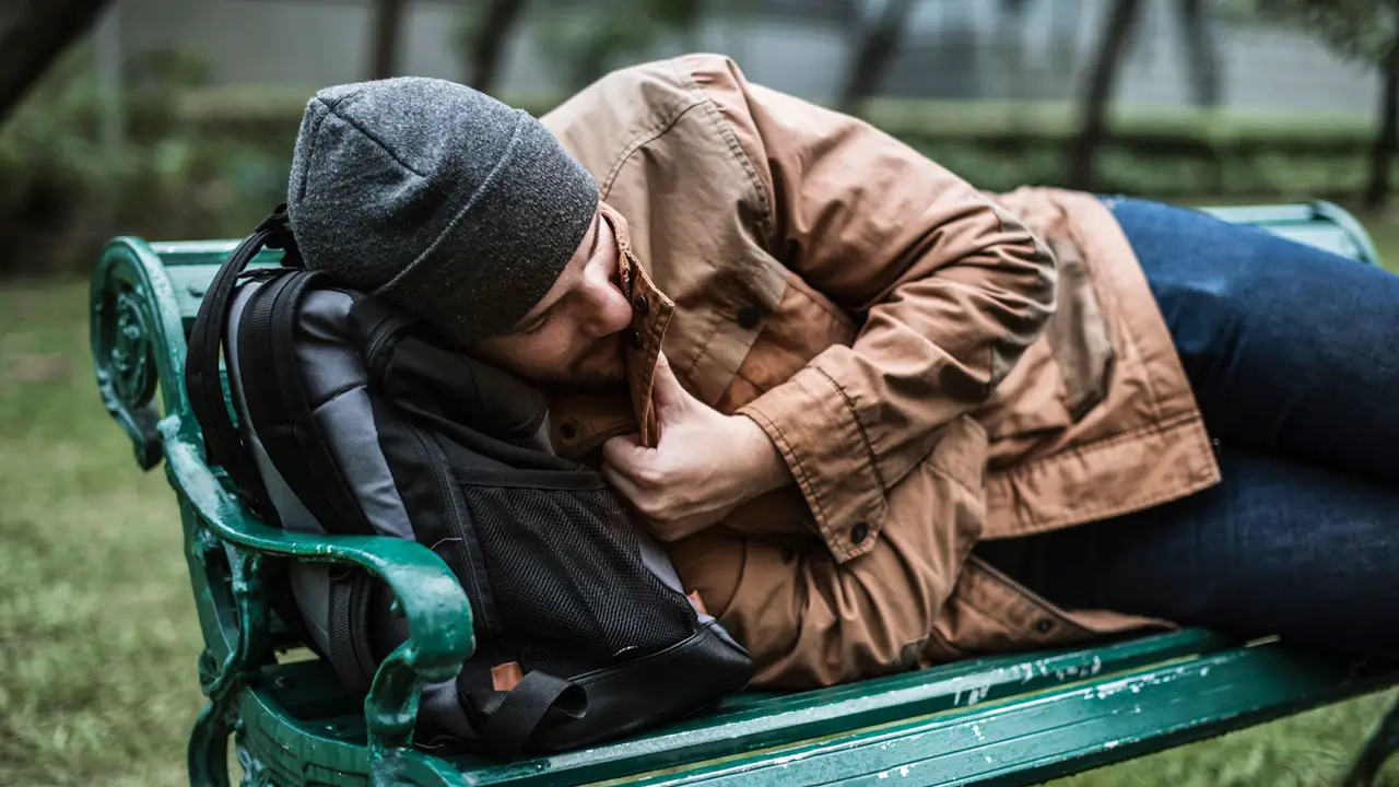 A homeless adult man sleeping on bench in the park