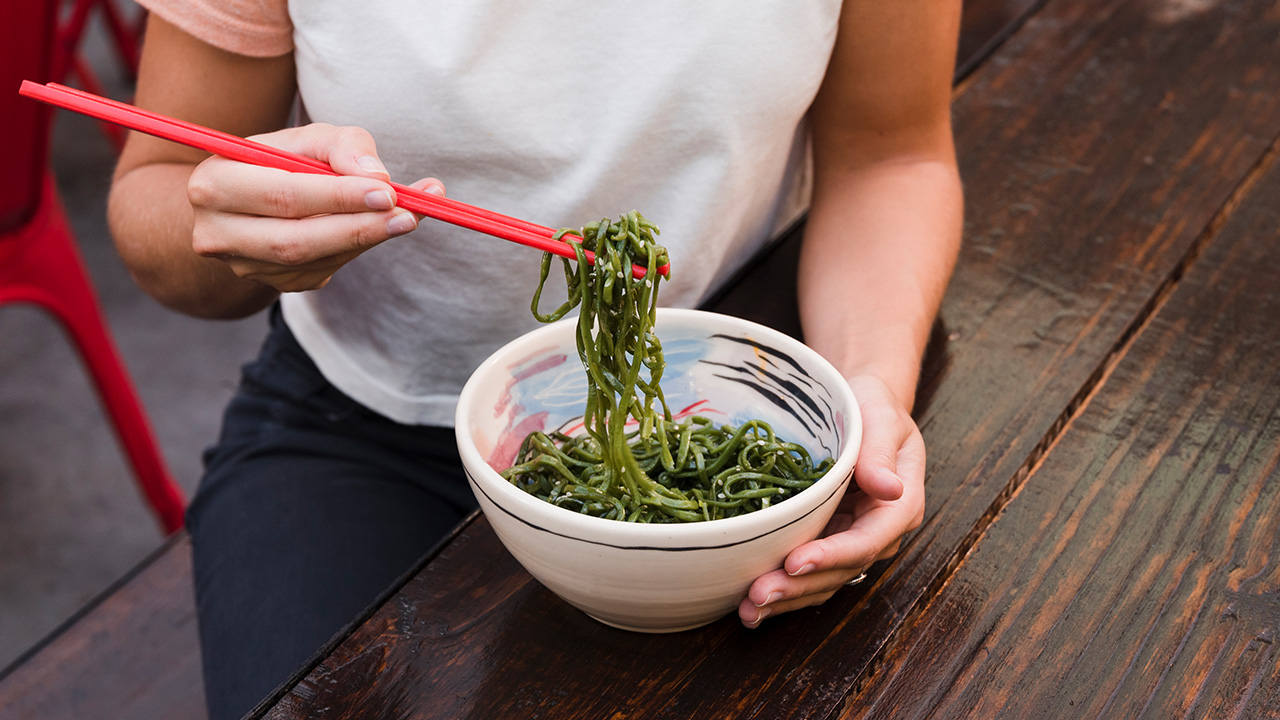 Close up of a womans hand eating green seaweed with red chopsticks