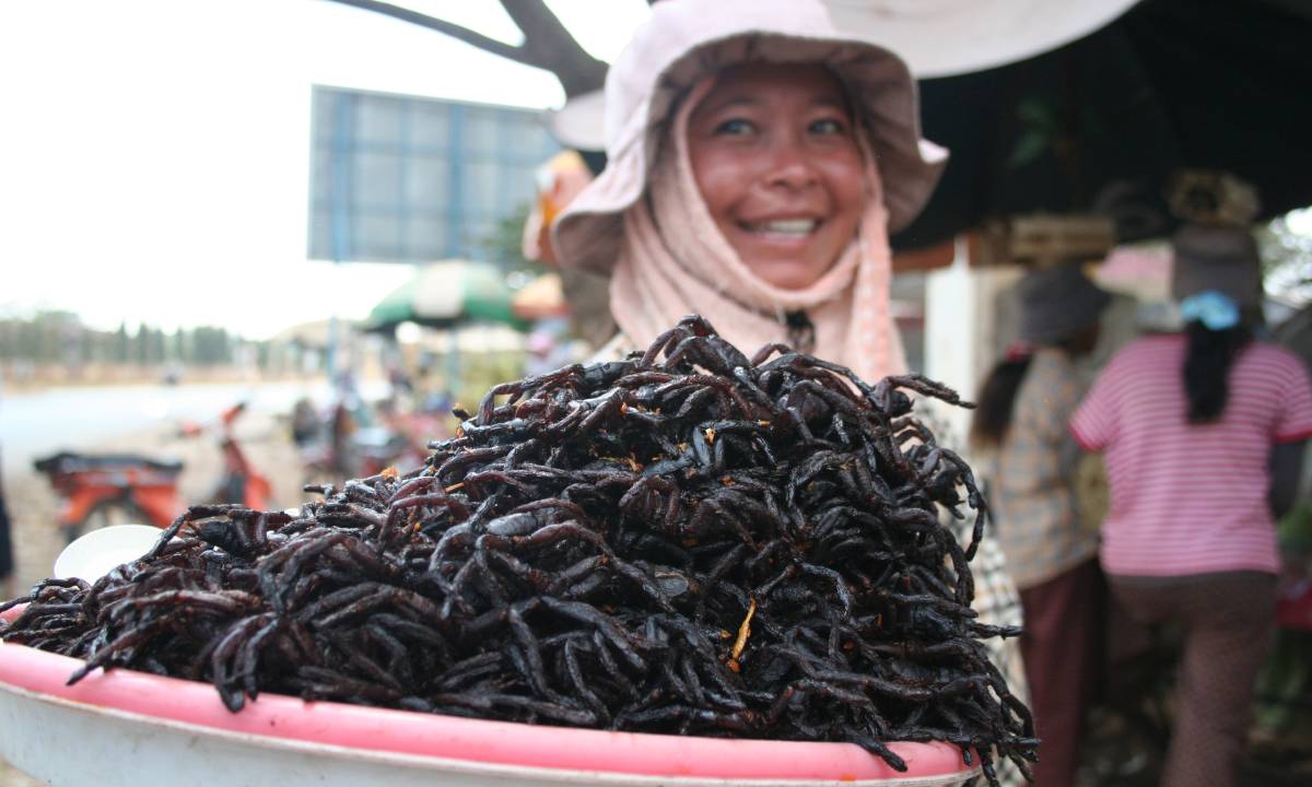 Happy woman onlooking a pile of fried spiders (Tarantula) in Cambodia